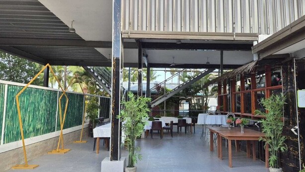 An outdoor dining area with tables and chairs, surrounded by potted plants and a staircase leading to an upper level. - Bluelight Village Hotel (Nadi)