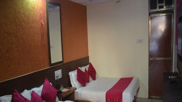 A hotel room with two beds, each with white bedding and red accents. There is a wooden headboard, a nightstand with a lamp, and a mirror on the wall.