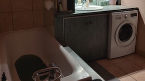 Et lille vaskerum med vaskemaskine, vask og et hylder med diverse toiletartikler.