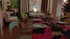 Et spiseområde med et bord dækket til fire personer, stole, en radiator, en sofa og en væg med et plakat.