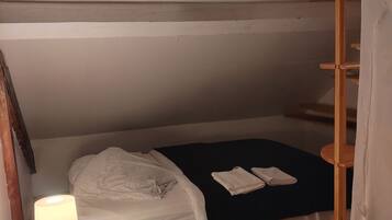 A small, cozy bedroom with a single bed, a bedside table with a lamp, and a wooden ladder.