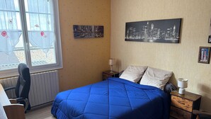 A bedroom with a bed, a desk, a chair, a window with curtains, a nightstand, and a lamp. - Bed and breakfast USA (Mayenne)