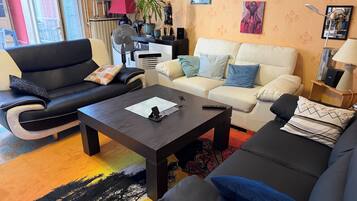 Ein Wohnzimmer mit einer schwarzen Ledersofa, einem weißen Sofa und einem Couchtisch. Dort steht eine Lampe, eine Pflanze und ein gerahmtes Bild an der Wand.