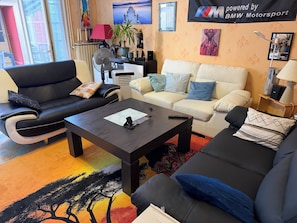 A living room with a black leather sofa, a white sofa, and a coffee table. There is a lamp, a plant, and a framed picture on the wall. - Bed and Breakfast in the U.S. at XAVIER's (Mayenne)