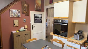 Een kleine keuken met een inbouwoven, een compacte koelkast en een houten eettafel met stoelen.
