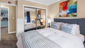 A hotel room with a large bed, a mirror, a bedside table, and a colorful abstract painting on the wall.
