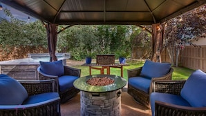 A covered patio area with wicker furniture, a stone fire pit, and a hot tub.