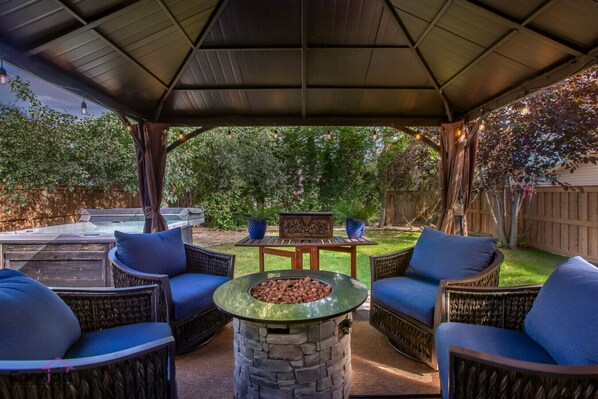 A covered patio area with wicker furniture, a stone fire pit, and a hot tub. - Modern Eclectic Home~Walk to WEM~AirCon~Yard~Hot Tub (Edmonton)