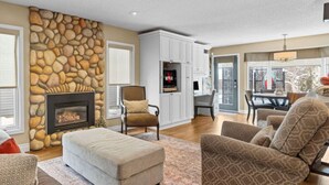 A living room with a stone fireplace, comfortable seating, and a view through a glass door.