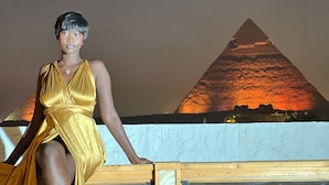 Kultainen mekko päällään oleva henkilö seisoo parvekkeella, jolta avautuu näkymä pyramidiin.