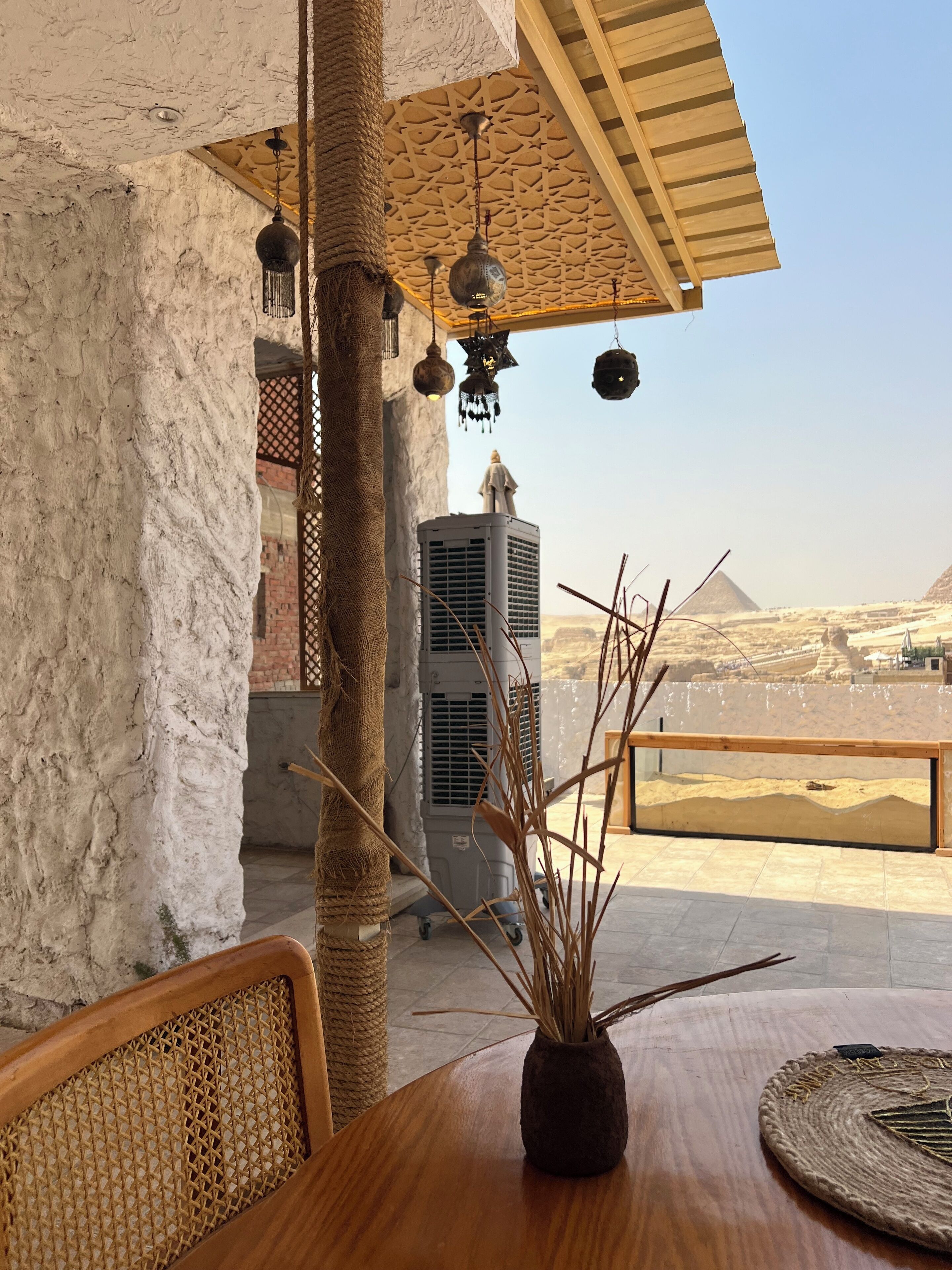 A wooden table with a woven basket and a vase with branches, a textured wall, and a view of pyramids in the background.