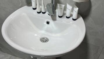 A white bathroom sink with a chrome faucet, a soap dispenser, and several tubes of body wash.