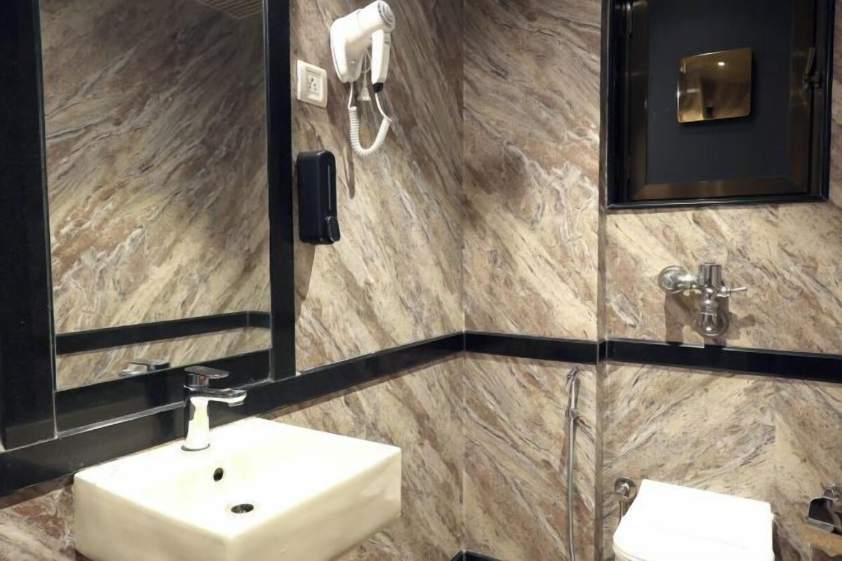 Un baño con pared de mármol, lavabo, espejo, secador de pelo y retrete.