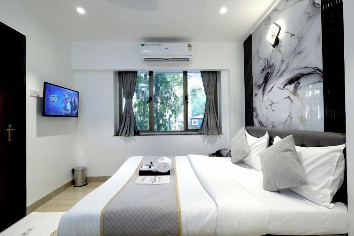 A modern hotel room with a large bed, a flat-screen TV, an air conditioning unit, and a window with curtains.