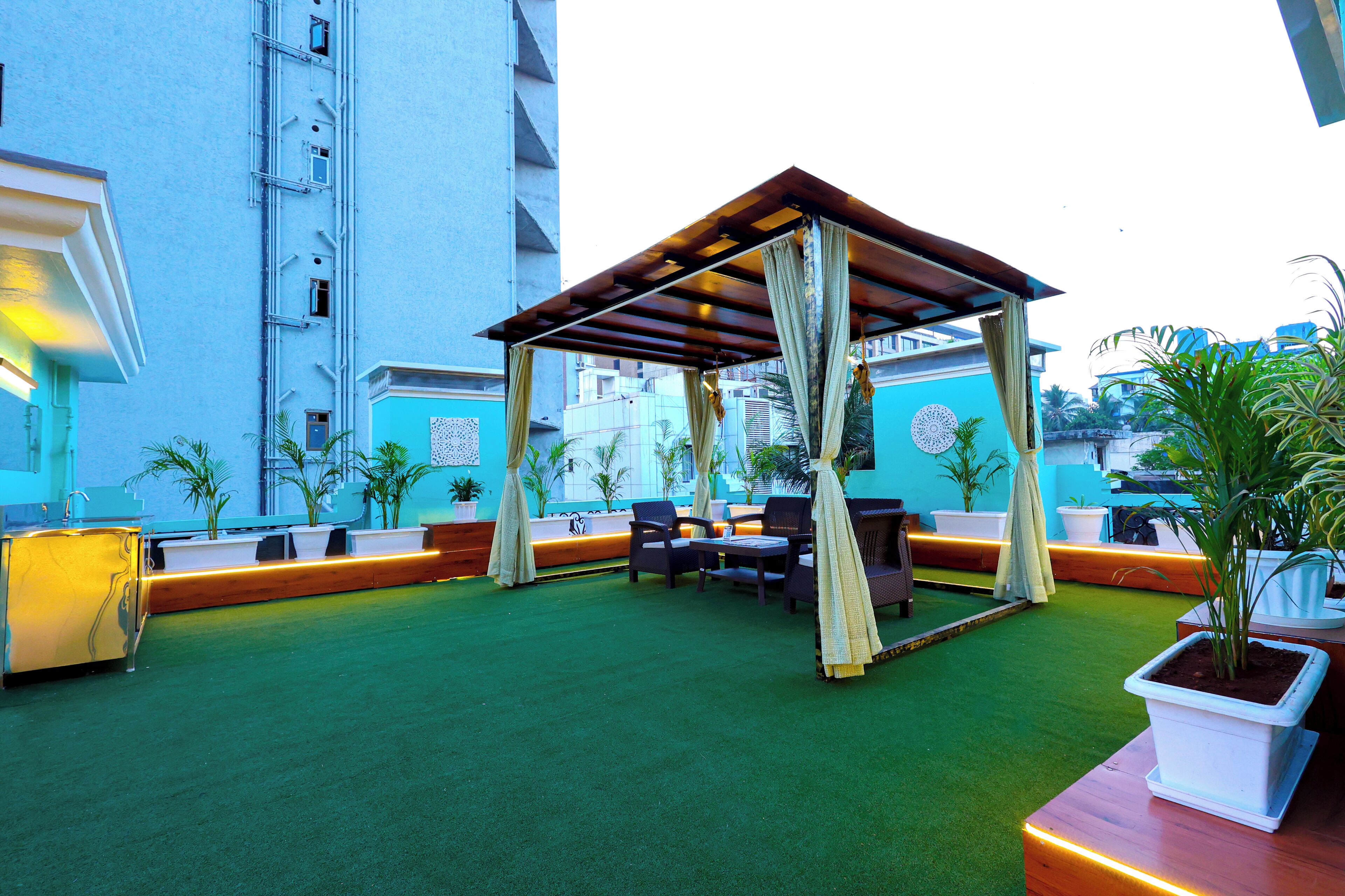 An outdoor seating area with a wooden pergola, green artificial turf, and potted plants.