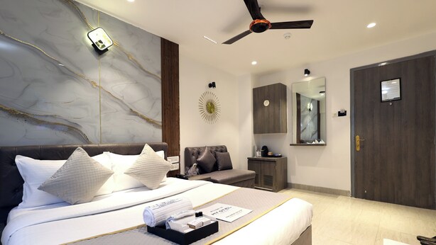 A modern hotel room with a large bed, a ceiling fan, a bedside table, a mirror, and a wardrobe. - MyOtel - Santacruz (Mumbai)