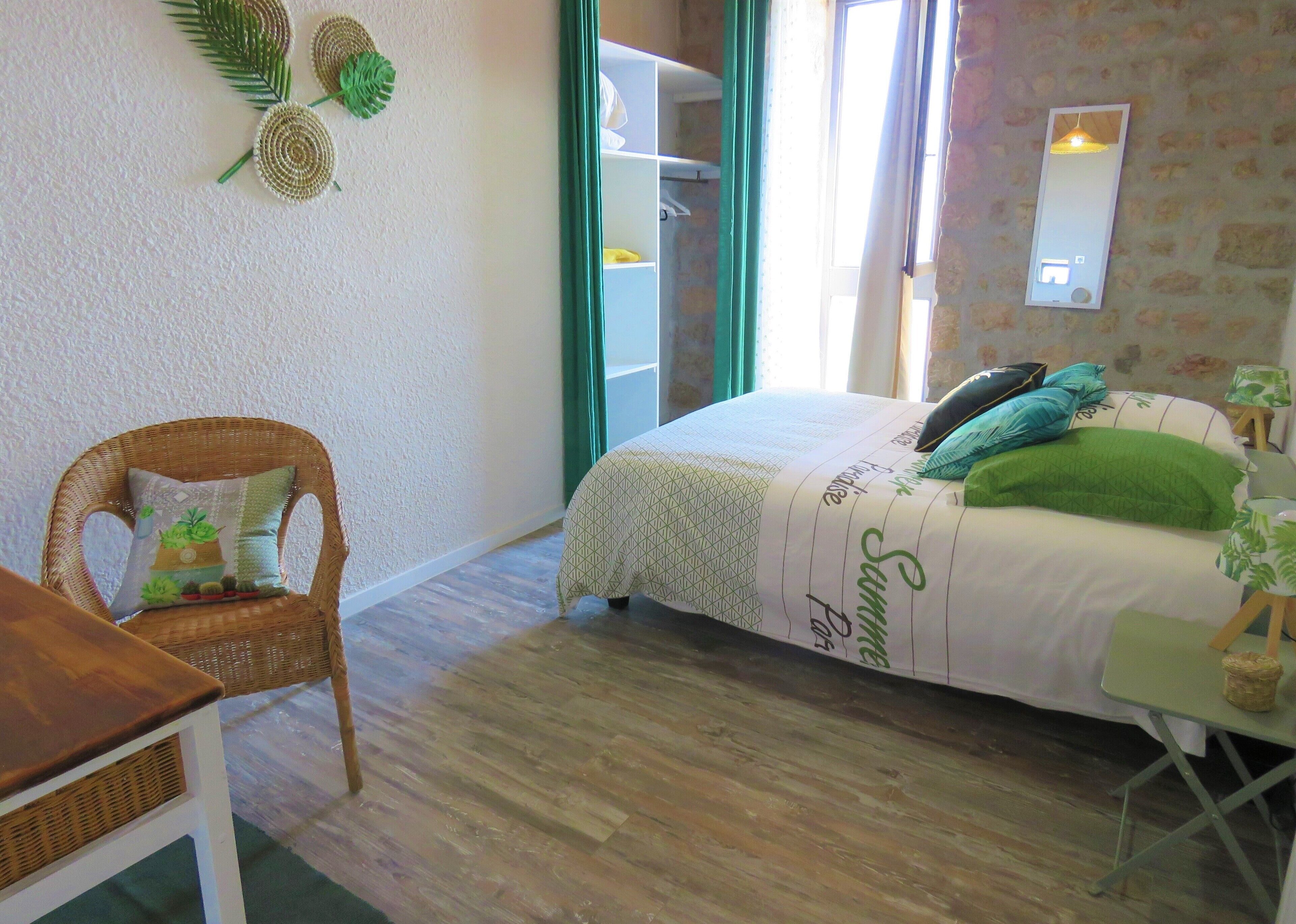 A bedroom with a bed, a chair, a small table, a mirror, and a window.