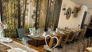 A restaurant with long wooden tables set for dining, a forest mural on the wall, and a heart-shaped centerpiece.