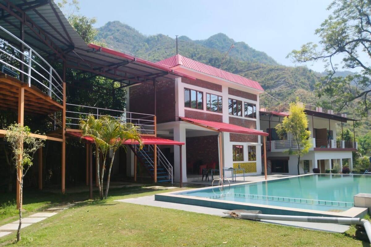 A two-story building with a swimming pool, surrounded by a grassy area and trees.