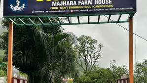 Un panneau indiquant « Buddy Hikers Majhara Farm House », et précisant les services offerts, tels que la restauration, l’hébergement, une piscine et un espace de camping.