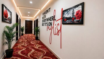 Un pasillo con alfombra estampada, plantas en macetas, obras de arte enmarcadas y una pared con una cita inspiradora.