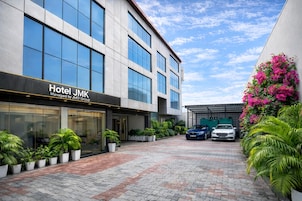 A modern hotel building with a glass facade, a paved courtyard, and parked cars.
