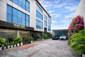 A modern hotel building with a glass facade, a paved courtyard, and parked cars. - Hotel JMK - Managed by JMD Group (New Delhi)