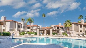 A pool area with lounge chairs and palm trees, surrounded by buildings with a Mediterranean architectural style. - Resort style condo in Scottsdale (Scottsdale)