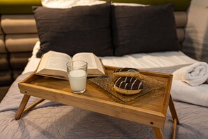 A wooden tray with a book, a glass of milk, and a chocolate-covered donut on a bed with a quilted cover. - Dream 19A Studio Przeszklona Azienka Centrum (Bydgoszcz)