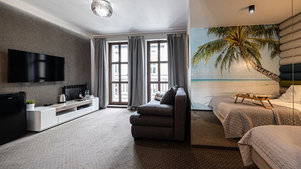 A modern hotel room with a flat-screen TV, a sofa, a bed, and a large window with curtains.