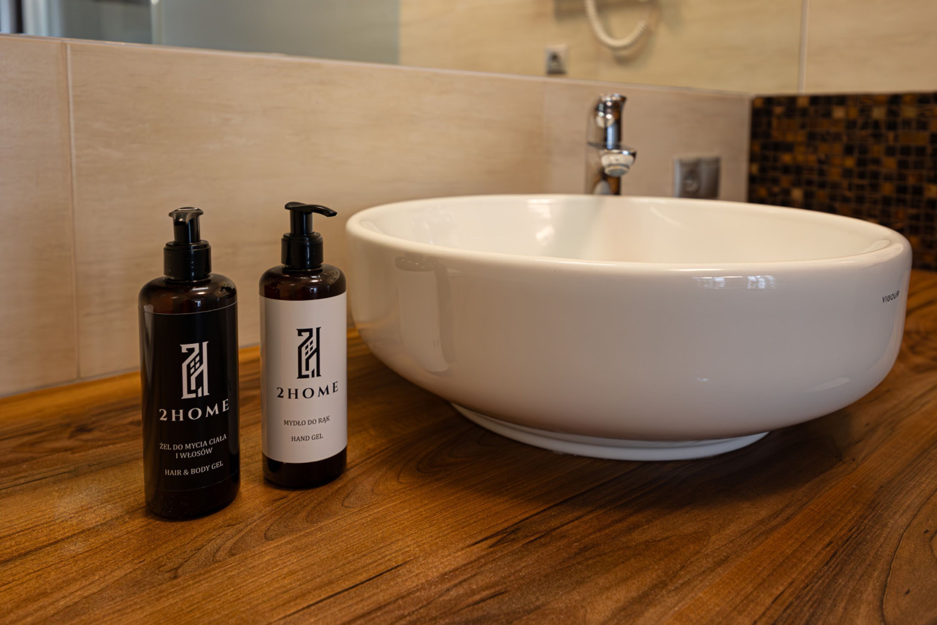 A bathroom with a white sink, two bottles of hair and body gel, and a wooden countertop.
