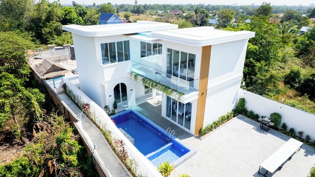 Een modern huis met twee verdiepingen, een glazen balkon, een zwembad en een tuin.