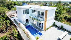 Una casa moderna de dos pisos con un balcón de vidrio, piscina y jardín.