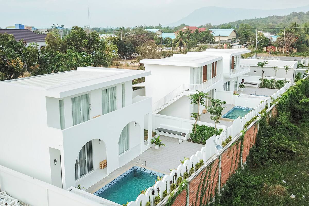 Een modern resort met meerdere witte gebouwen, een zwembad en uitzicht op verre bergen.