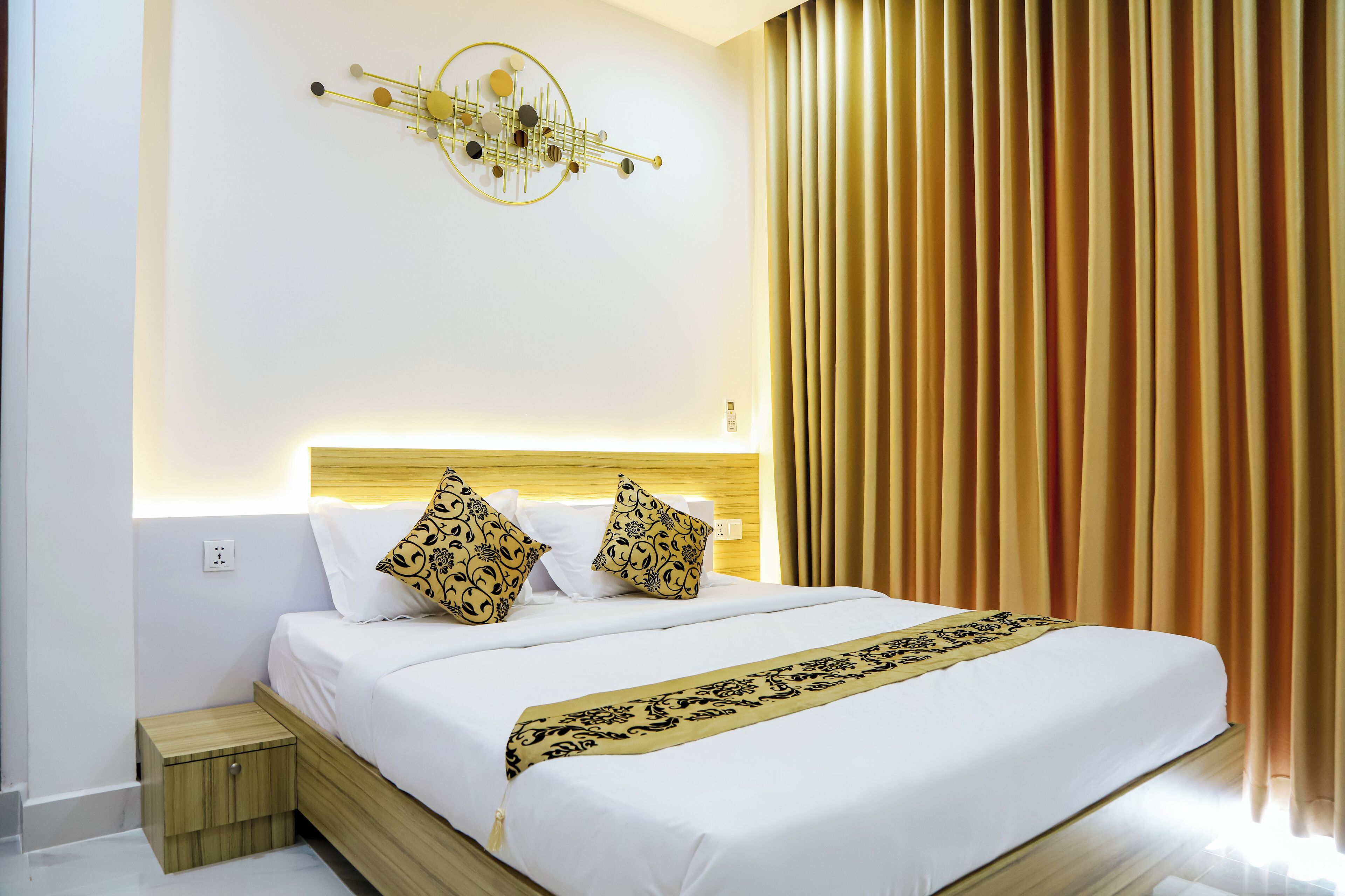 A neatly made bed with white linens and decorative pillows, a bedside table, and a wall-mounted light fixture.
