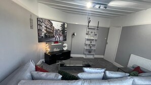 A modern living room with a grey sofa, a flat-screen TV, and a decorative shelf. - Home Away From Away. Charming 2-bedroom apartment in wonderful Croydon with WiFi (Croydon)