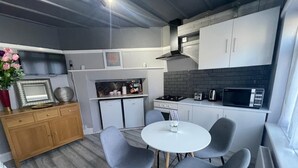 A compact kitchen with a dining area, featuring a white table and grey chairs, a small fridge, and a microwave. - Home Away From Away. Charming 2-bedroom apartment in wonderful Croydon with WiFi (Croydon)