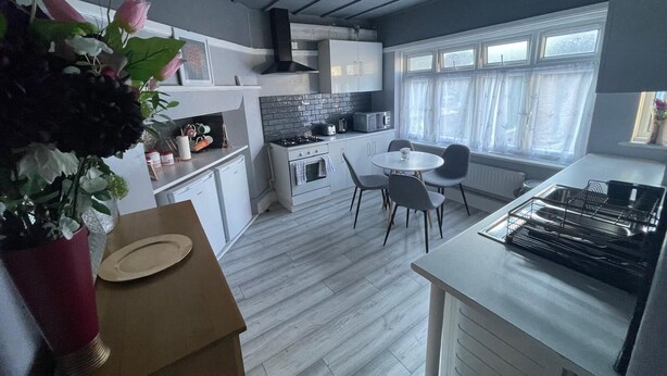 A modern kitchen with white cabinets, a gas stove, and a dining area with a round table and chairs. - Home Away From Away. Charming 2-bedroom apartment in wonderful Croydon with WiFi (Croydon)