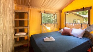 A bed with a dark blue bedspread, a wooden shelf unit, and a window with a view of trees. - Luxury Lodge for 5 people (Ghisonaccia)