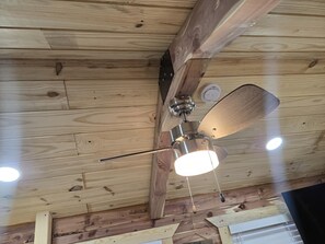 A ceiling fan with a light fixture is mounted on a wooden beam in a room with exposed wooden beams and a sloped ceiling.