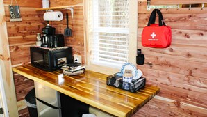 A compact kitchen with wooden walls, a coffee maker, a microwave, and a first aid kit on the wall. - #4 - Amish Log Camping Cabin Walk To The Water Cabin (Toronto)