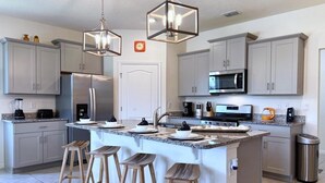 A modern kitchen with a central island, stainless steel appliances, and wooden stools. - Beautiful 5 Bed Pool Home With Game Room-7543ol 5 Bedroom Home (Davenport)