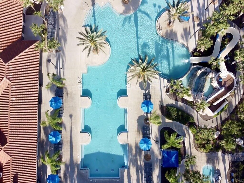 Vista aèria d'un complex amb piscina central, palmeres i zones de relaxació.