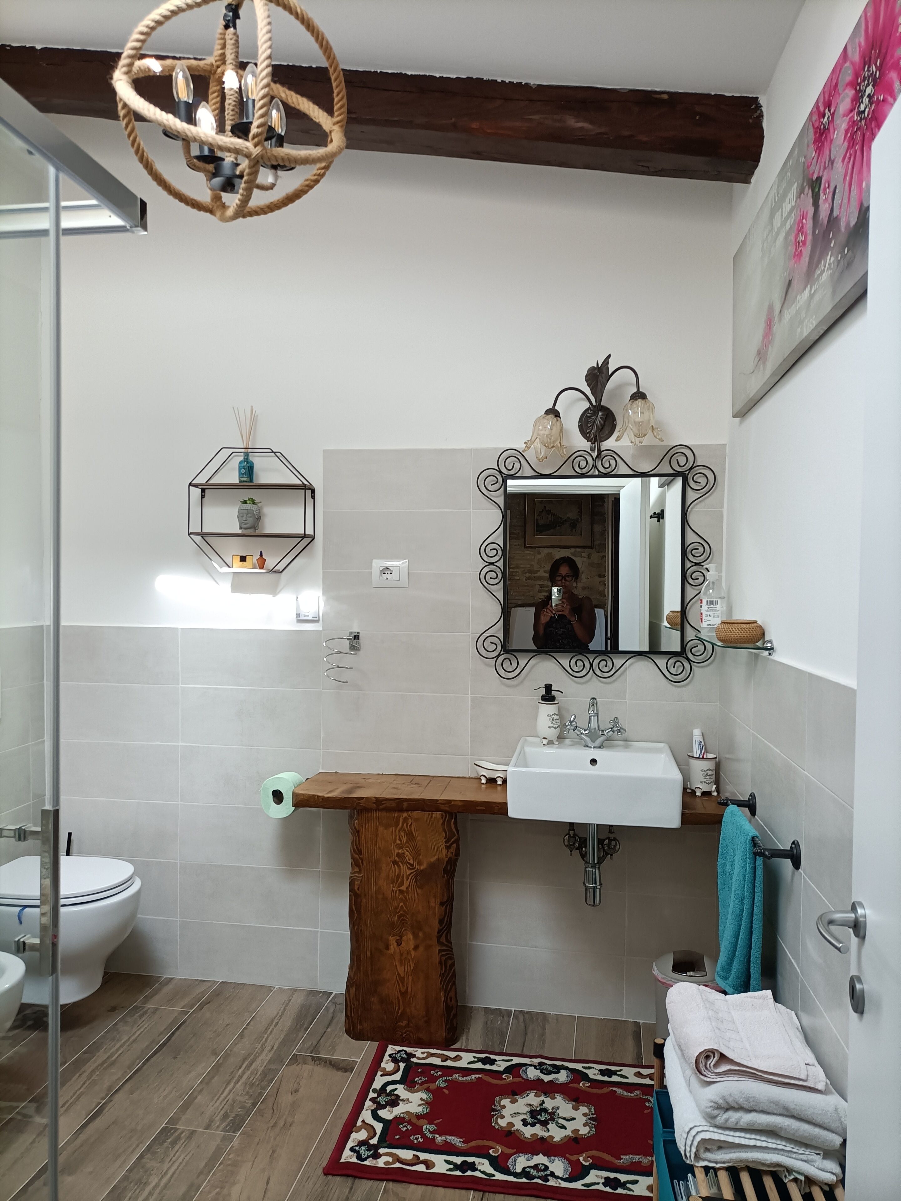 A bathroom with a wooden vanity, a white sink, a mirror with a decorative frame, a hanging light fixture, and a tiled floor.