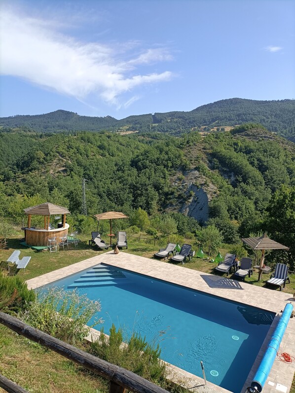 A pool area with lounge chairs and a bar, surrounded by lush greenery and hills.