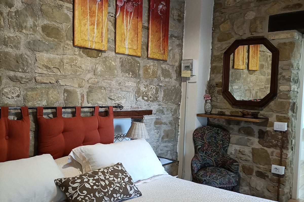Une chambre avec un mur en pierre, un lit avec des oreillers rouges et blancs, et une couverture colorée.