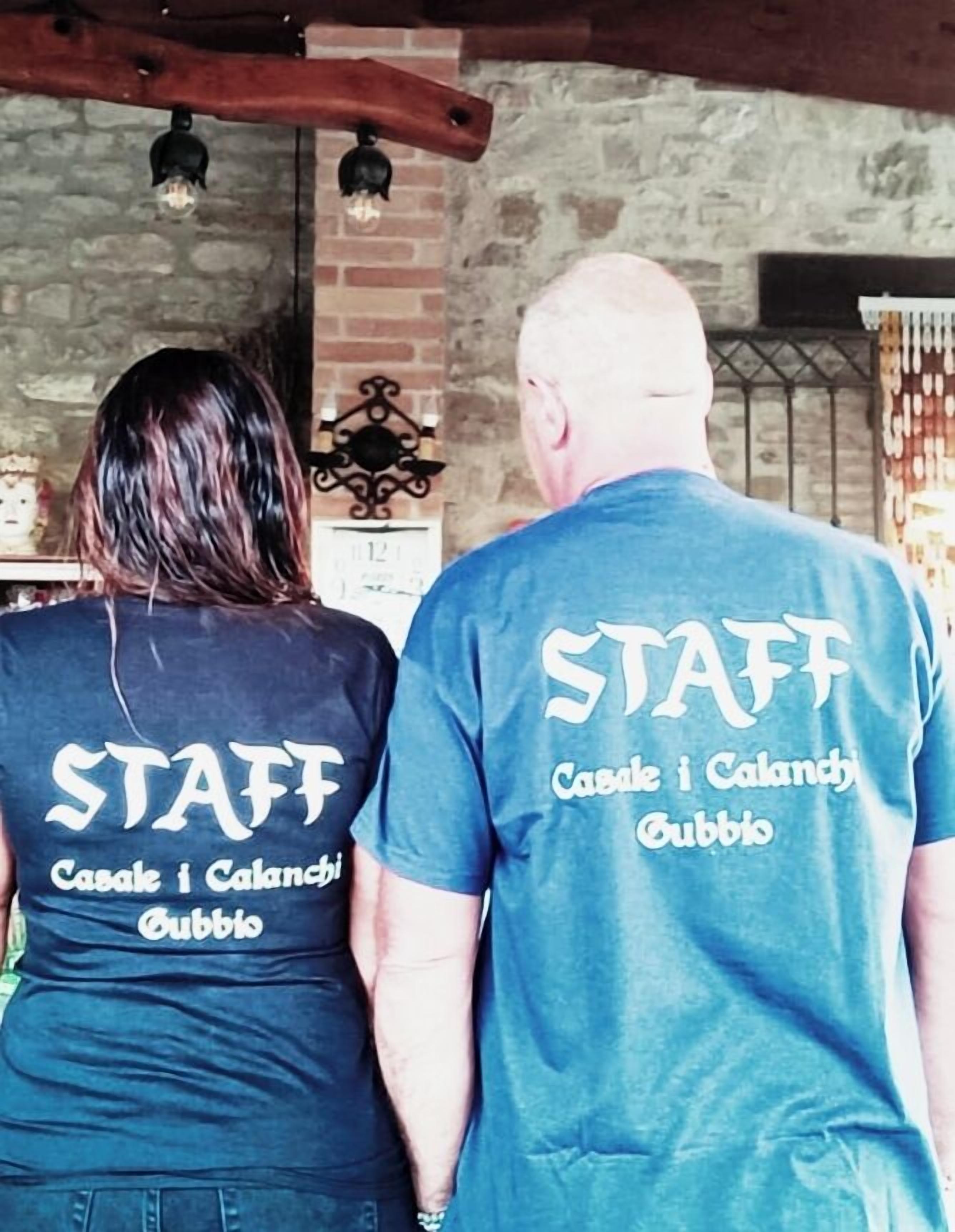 Two people wearing matching t-shirts with "STAFF" and "Casale i Calanchi Gubbio" printed on the back.