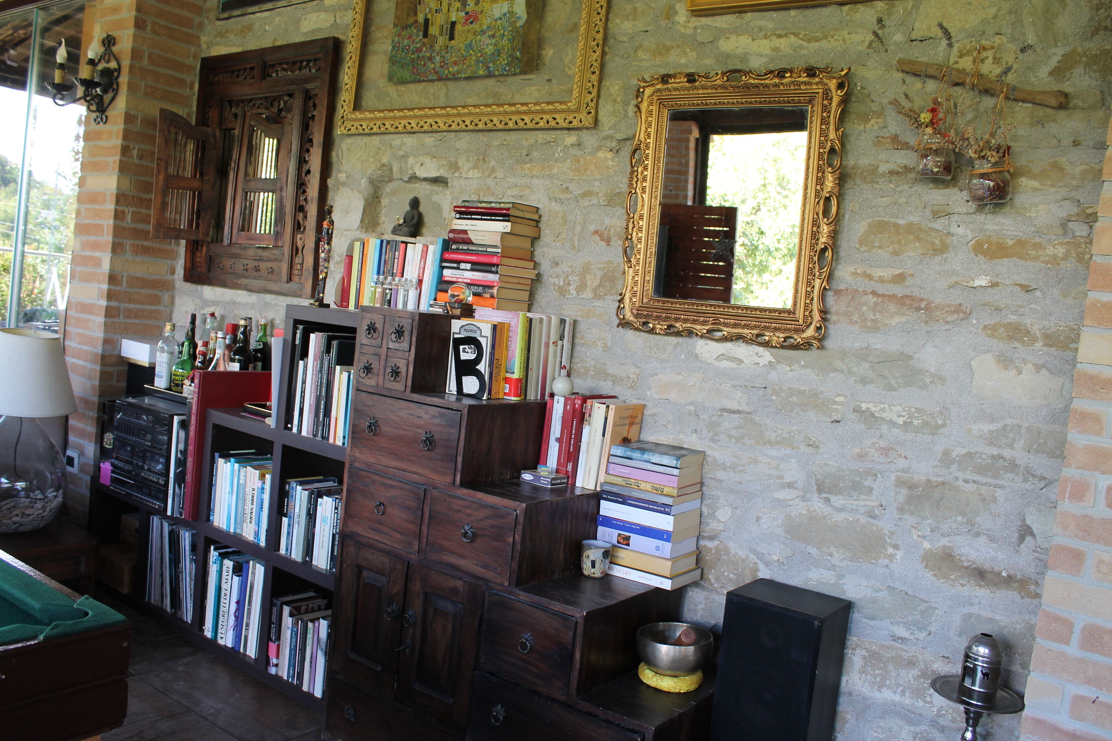 A room with a brick wall, wooden bookshelves, a mirror, and a small table with a bowl.