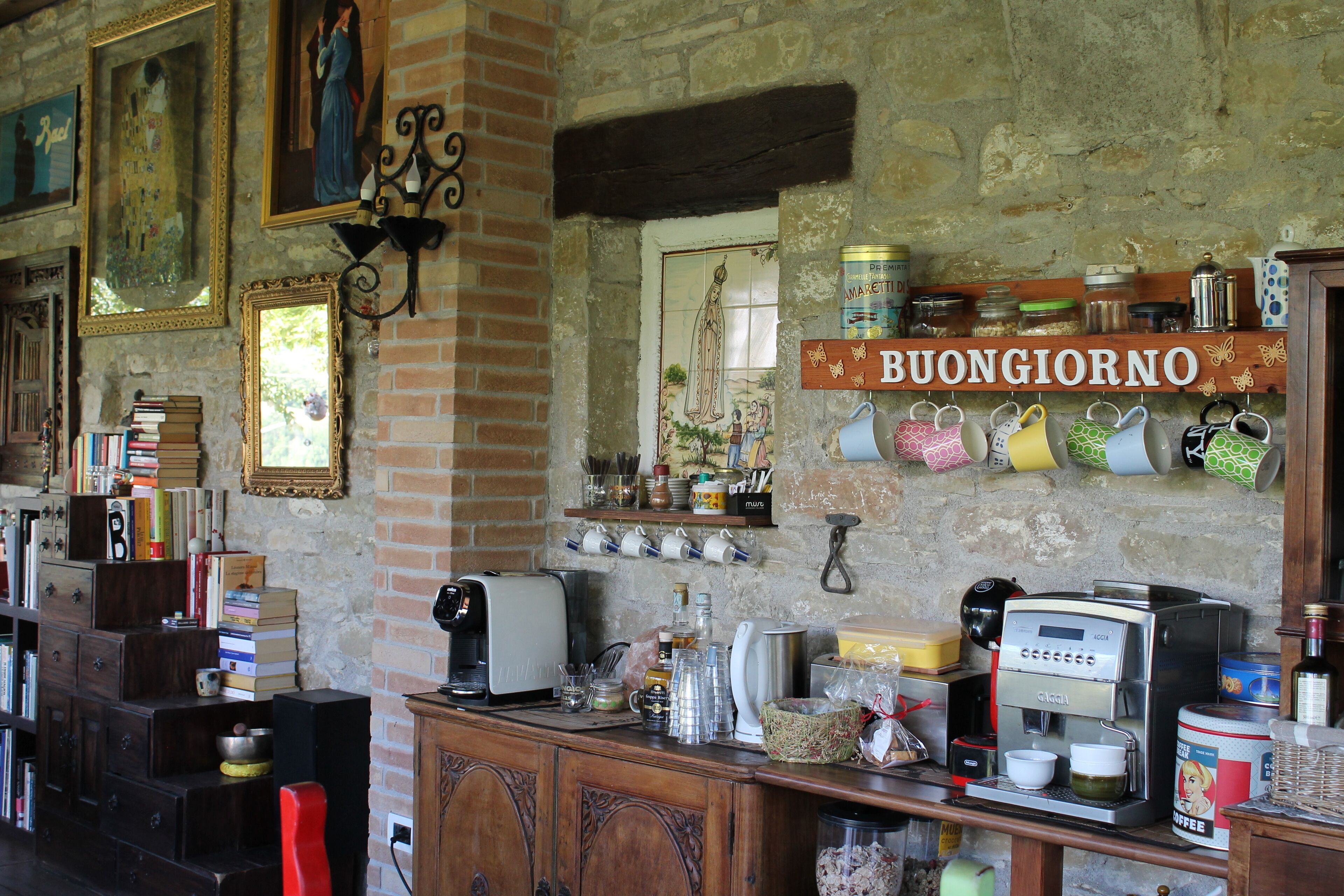 Une cuisine rustique avec une machine à café, des étagères remplies de bocaux et une pancarte indiquant « BUONGIORNO ».
