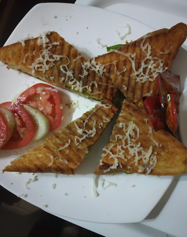 A white plate with triangular pieces of food topped with shredded cheese, accompanied by sliced tomatoes and cucumbers.